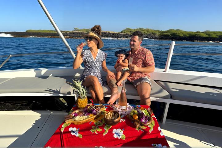 Family enjoying snacks on a boat with ocean and island in background.