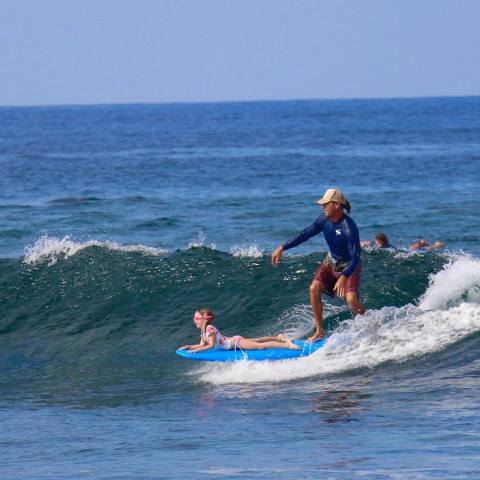 Guy Surfing With Girl Lying On Surfboard