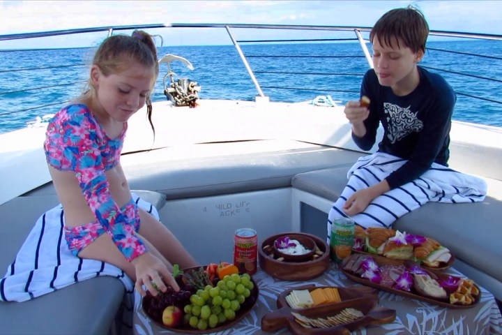 Two children enjoy snacks on a boat, with ocean in background.