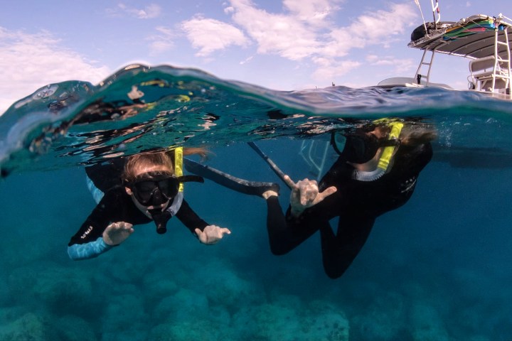 Two children enjoy snorkeling during Kona day camp for kids. Shot is halfway underwater and halfway above the water