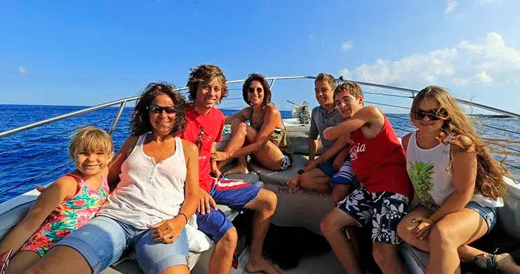 Group of seven people smiling on a boat in sunny weather.