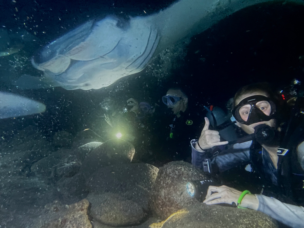 A group of scuba divers swims underwater, posing for a photo with manta ray in Kona, Hawaii.