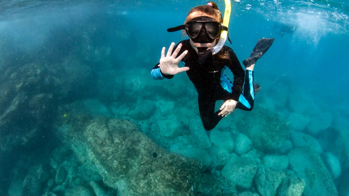Young child snorkeling underwater in Kona, HI. She waves at the camera.