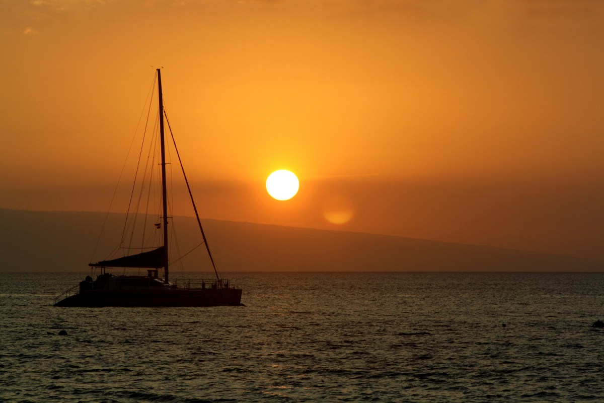 Sailboat floating in bay at sunset off coast of Kona, Hawaii.
